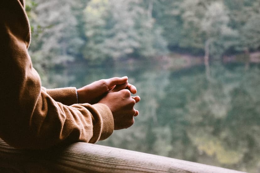 arms held pensively on a rail before a blurred background of trees and a lake