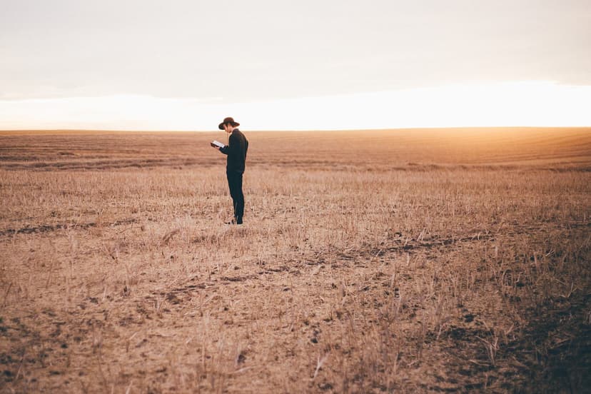 lone man standing out in a wheat field plain holding a book